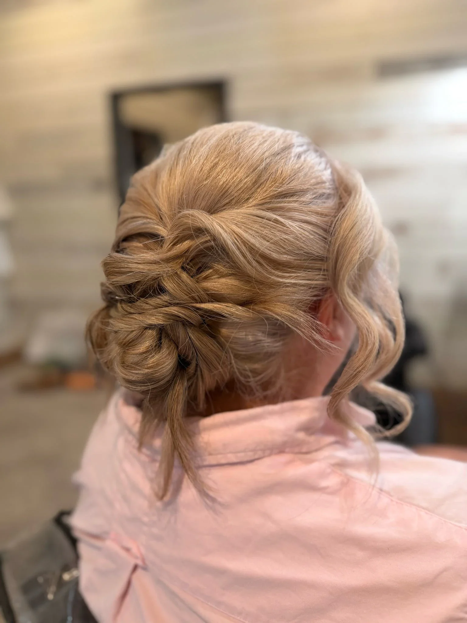 Side-back view of a blonde braided low updo with curled tendrils