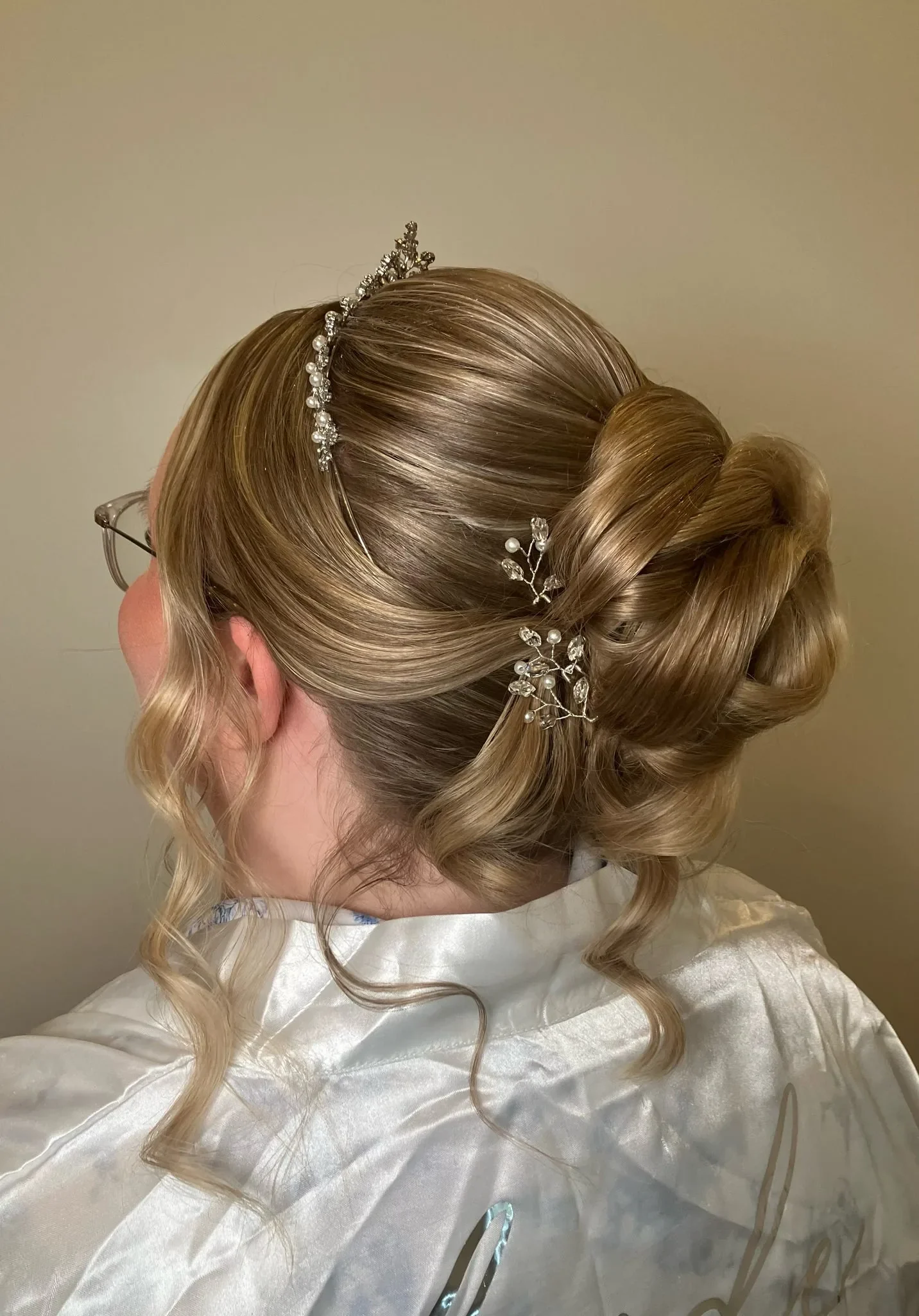 Blonde looped bridal updo with a pearl tiara and crystal hair pins by Glow Salon & Spa