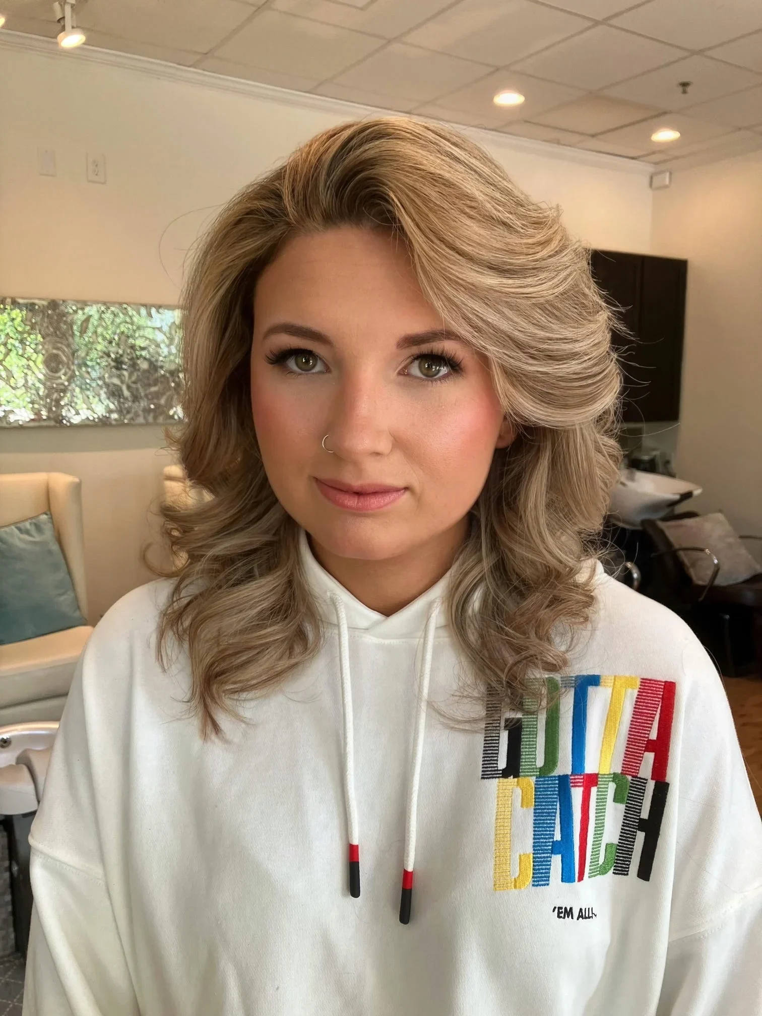 Blonde bridal hairstyle with voluminous side-swept curls and soft-glam makeup by Glow Salon & Spa in Carmel, Indiana