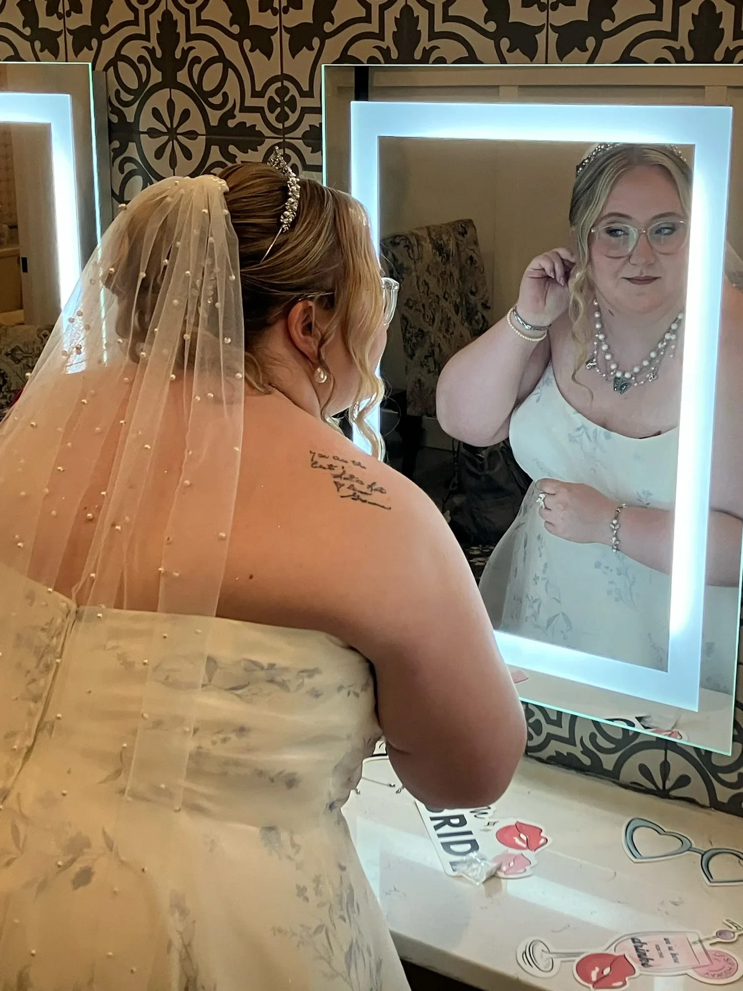 Bride wearing a pearl veil, tiara updo, and polished wedding makeup in a mirror portrait