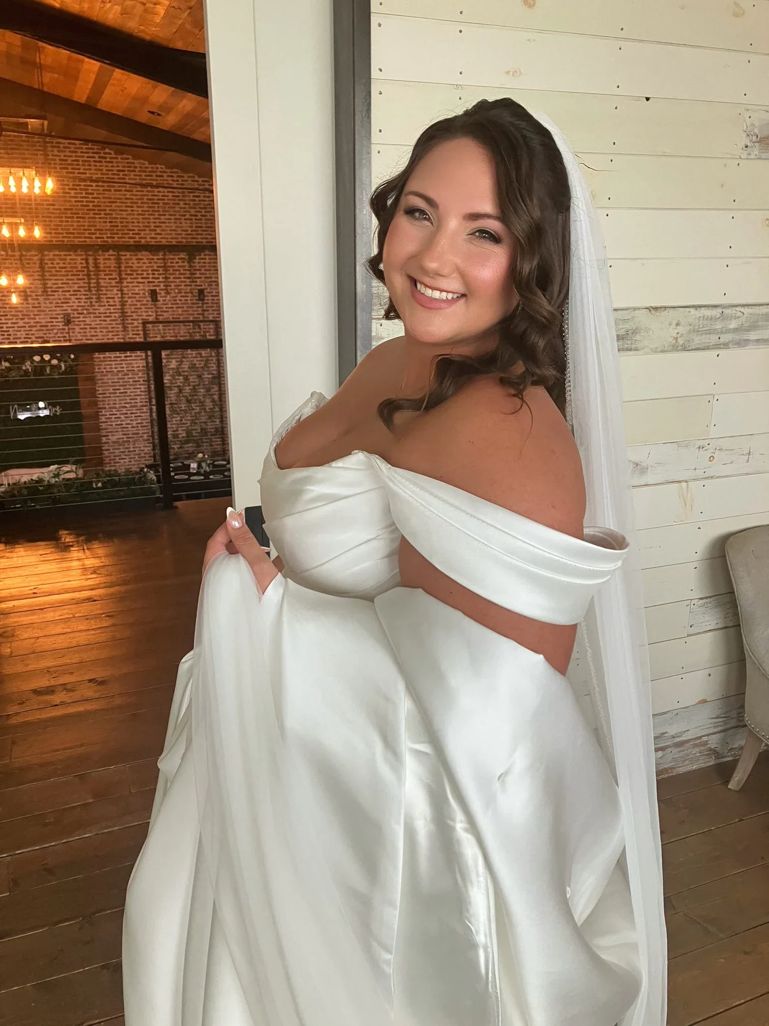 Bride in an off-the-shoulder gown with brunette waves, veil, and soft-glam makeup by Glow Salon & Spa